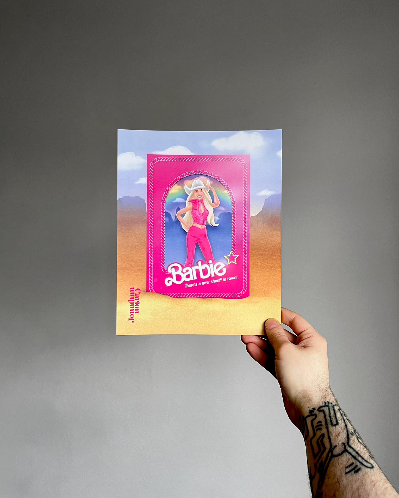 Hand holding an art print with a Barbie design against a gray background