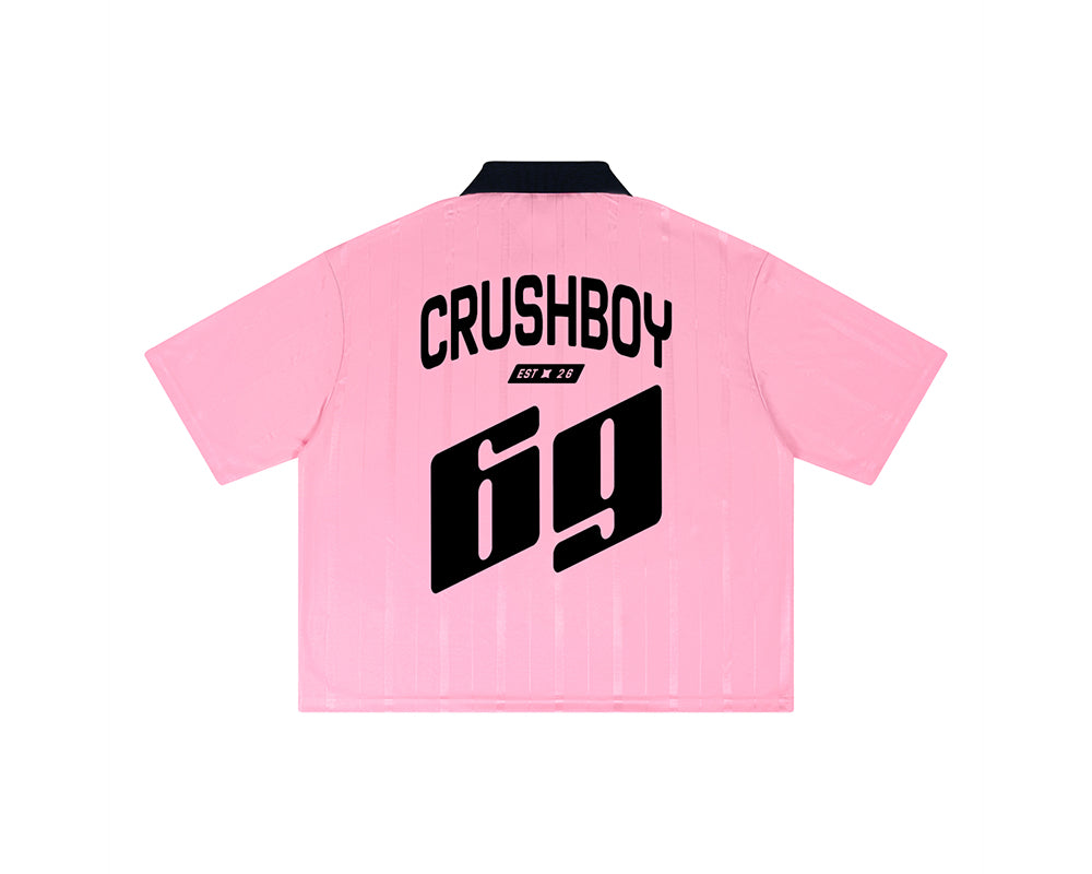 A light pink short-sleeve polo shirt shown from the back, featuring a black collar and bold black text reading 'CRUSHBOY' with 'EST. 26' above a large '69' graphic.