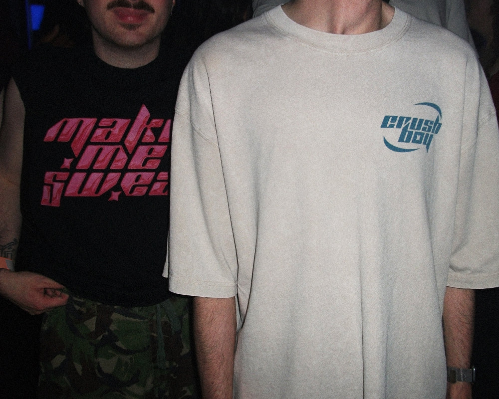 A person wearing an oversized off-white t-shirt with a blue 'crushboy' logo on the chest, standing next to another person in a black graphic shirt.