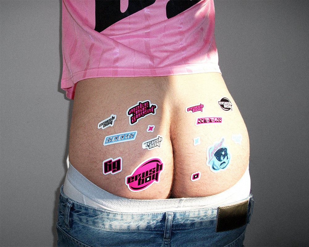 Rear view of a person wearing a pink shirt and blue jeans, with multiple colorful novelty stickers applied to the buttocks against a plain gray background.